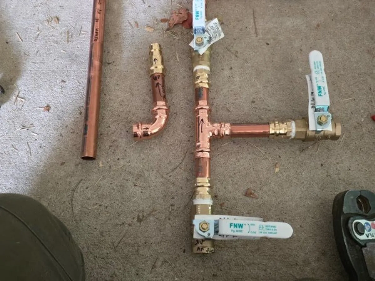 Copper manifold assembly with soldered tees, elbows and four labelled brass ball valves, laid out before installation.