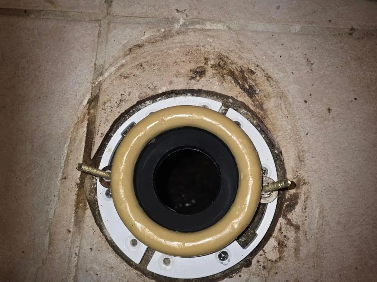Toilet closet flange bolted to the tile floor with a new wax ring seated and closet bolts set for the toilet to drop onto.