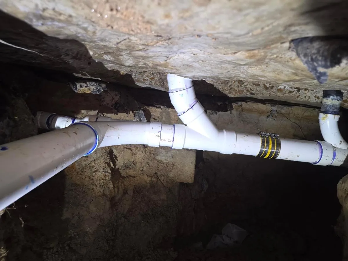 Replacement PVC drain line with a wye fitting, installed in a tunnel dug under a slab foundation.