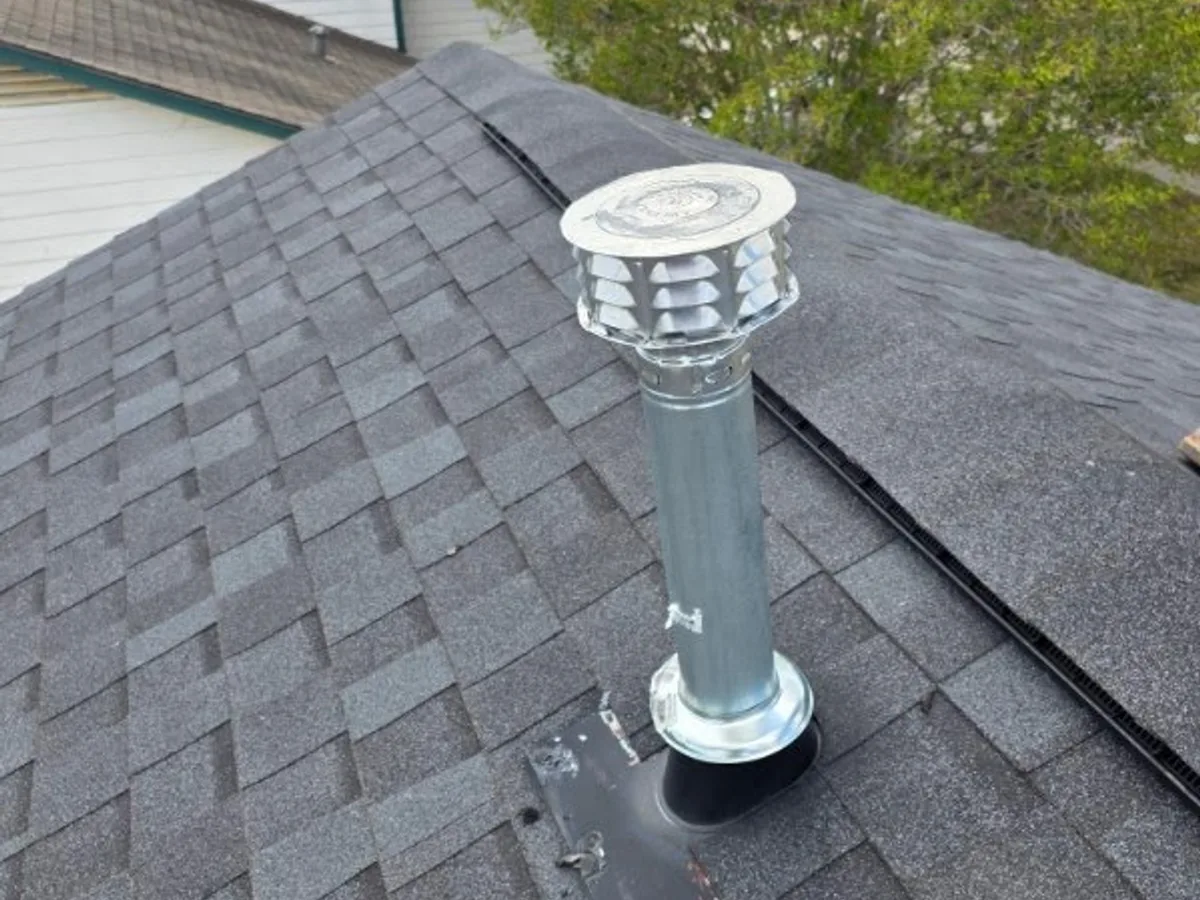 New galvanised water heater flue and rain cap through a shingle roof, sealed with a fresh rubber boot flashing.