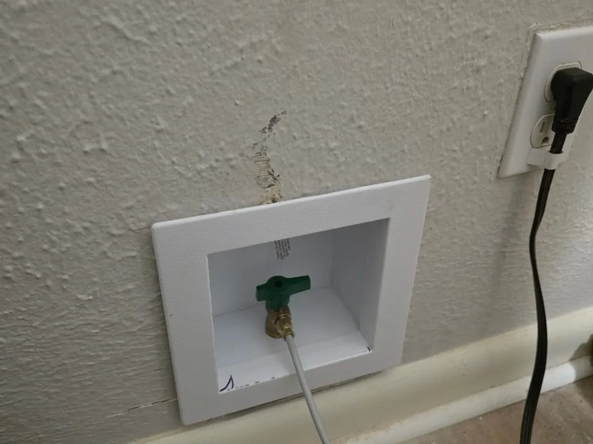 Recessed washing machine outlet box installed in a wall with a quarter-turn valve and supply hose connected.