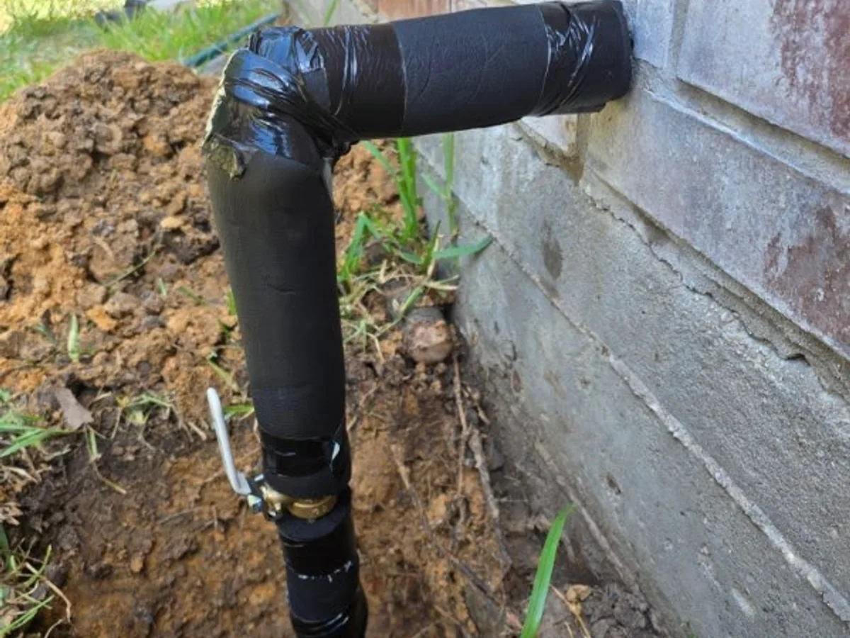 The same water line riser after wrapping — pipe and fittings insulated and taped for freeze protection above ground.